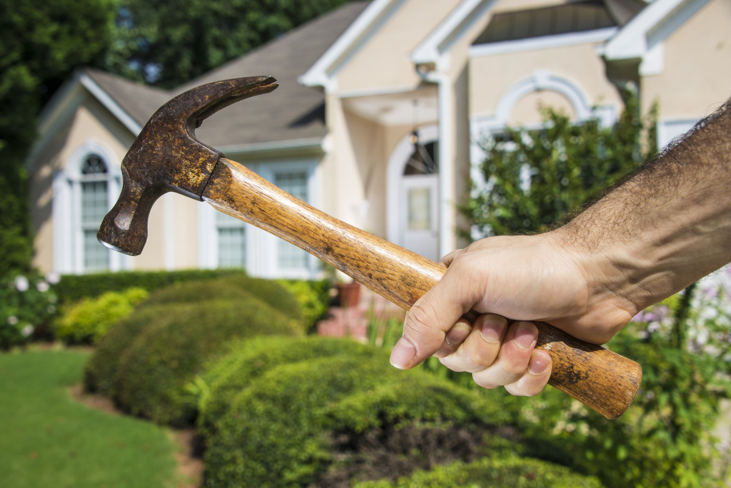 man holding hammer in front of house representing home maintenance